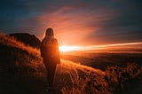 A woman lets go of her thoughts while watching a sunset in the countryside