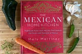 ‘The Mexican Home Kitchen’ cookbook, shown on a bamboo cutting board with fresh chiles, garlic, thyme and a carrot