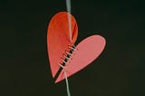 A severed paper heart being sown together.
