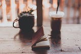 A wooden table with a small journal, a plant, and an iced coffee drink on top of it.