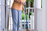 A woman sweeps the porch of her home.