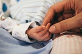 A parent holds the tiny hand of a newborn baby.