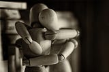 Sepia toned image of two wooden artist’s mannequins wrapped in an embrace