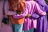 Back view of four women with arms round each other, wearing purple tops
