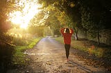 Person resting both hands on the head, standing facing the sun in a park or trail.