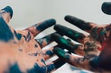 Two hands, palms up, covered in dark blue, black, and green pigments.