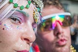 zoomed into faces of two glitter filled faces with colorful acessories