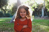 Happy Little Cute Girl With Curly Brown-Black Hairs! Background is a natural green park.