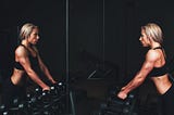 Fit blond woman holding weights and looking at herself in a gym mirror