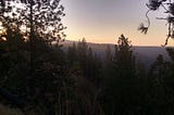 A scene of sunrise over trees with hills in distance