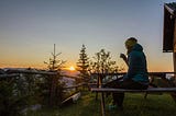 picture of a lady dressed in a jacket with a cup of cofee watching the sunrise