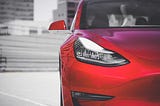 A red sporty car with high rise buildings in the background.