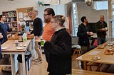 Two photos showing groups of adults standing around an office kitchen chatting and eating pastries