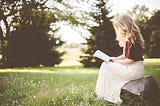 A girl reading a book/journal, out in the wild, in a field