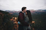 A couple standing close together, with the man gently kissing the woman on her forehead.