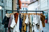 Assortment of clothing hanging on a dress rack on a city street, as if for consignment sale.