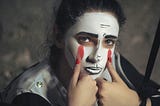Person in mime make-up drawing red tears down their face