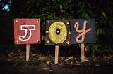 Three signs next to each other, spelling out the word “Joy”