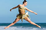 fit and free woman doing a ballet leap on the shoreline