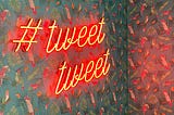 A wall with parrot wallpaper and a neon sign that says “#tweet tweet”