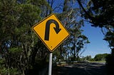 Yellow road sign with black curved arrow indicating turning around.