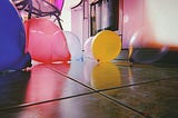 An array of balloons is spread out on a tile floor, a red, yellow, blue, and white one