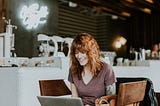 A young red-haired woman sitting in a coffee shop and working on a laptop