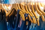 Identical blue tops hanging on a row of wooden hangers.