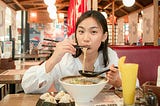 Lady eating ramen noodles in a restaurant with chopsticks.
