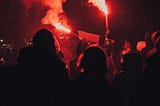 A crowd holding red flares