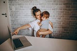 Woman holding child and pointing at a laptop.