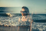 A woman stands by the sea, her silhouette blending with the waves in a double-exposure effect. The image captures both strength and vulnerability, reflecting the journey of overcoming life’s challenges with calm determination.
