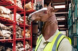 A horse-headed “reverse-centaur” whose eye has been replaced by the glowing eye of HAL9000 from 2001: A Space Odyssey. They are wearing a hi-viz vest and posed in shelving-aisles of an industrial warehouse.