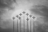 Jets surge skyward in a perfect arrow, smoke trails forming a sharp spearhead in the clouds, a monochrome symbol of teamwork, leadership, progress and upward momentum.