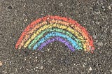 A photo of a rainbow painted in chalk on a pavement.