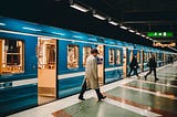A man in a trench coat exits a blue train into a very clean metro station.