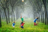 A group of boys play with a ball in a forest clearing.