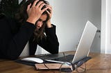 woman looking stressed sitting at her laptop with hands on her head