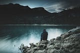 A person sits alone at a lake