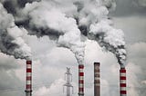 Image of red and white chimneys pumping smoke into the air from a power plant