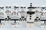 6 star wars storm troopers stand around 1 clown. they look similar, but the troopers suspect an imposter…