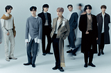 Members of the K-Pop group GOT7 stand in front of a light blue background in dark to neutral shade suits.