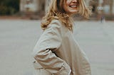 woman looking over her shoulder laughing with a long beige trench coat