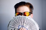 A young man with glasses holding a lot of money in his hands