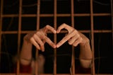 A person behind bars forming a heart with their fingers