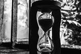 Life is short. Treasure every moment. Vintage hourglass, sand running out, blurred background, dramatic lighting.