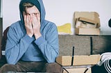 Man sitting at desk wearing hoodie, background messy. His hands are covering his face, fingertips pressing into his eyes. Is he possibly wondering what he’s gotten himself into, this time?