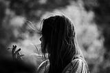 Black and white image of a woman in profile and shadow, smoking a cigarette, surrounded by smoke and mist.