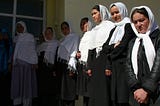 Afghan schoolgirls wearing black dresses and white head scarves. Lined-up to get into class.