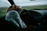 Woman has her head on the steering wheel of an unknown car, as if she’s crying.